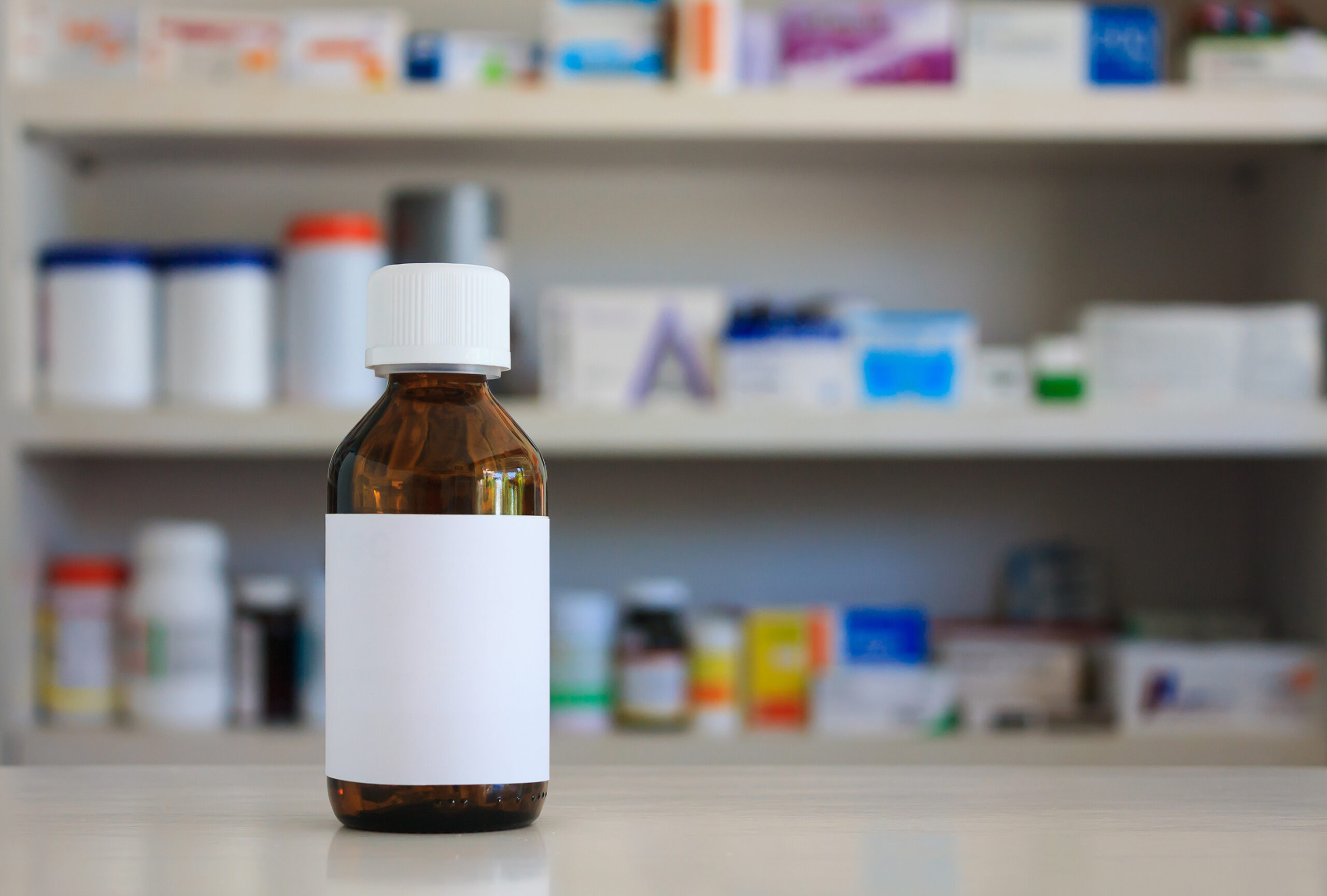 Blank white label of brown glass medicine bottle with blur shelves of drug in the pharmacy drugstore background